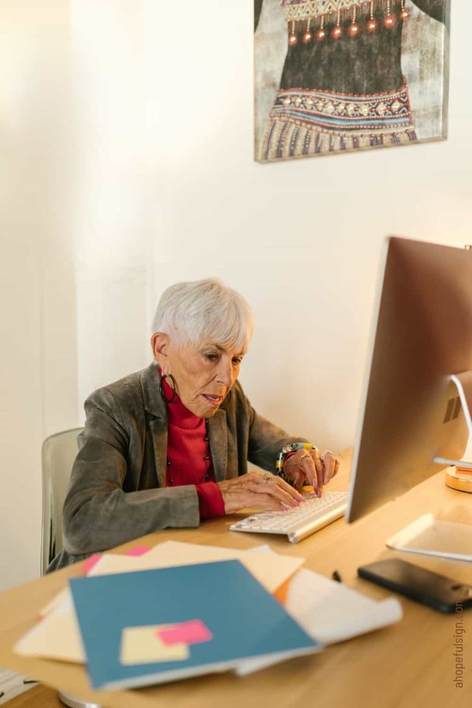 elderly woman in gray blazer typing on computer keyboard