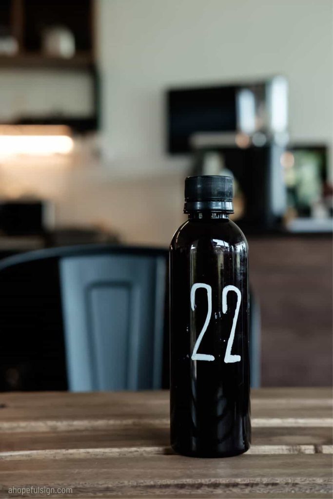 The number 22 written on a black bottle sitting on a wooden cafe table.