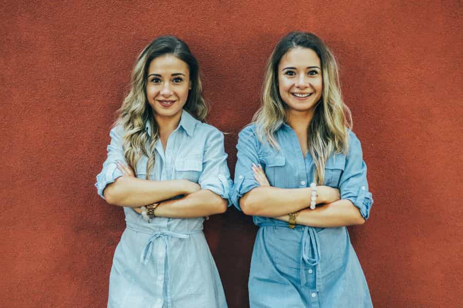 Twins standing with their arms crossed in front of a wall outdoors.