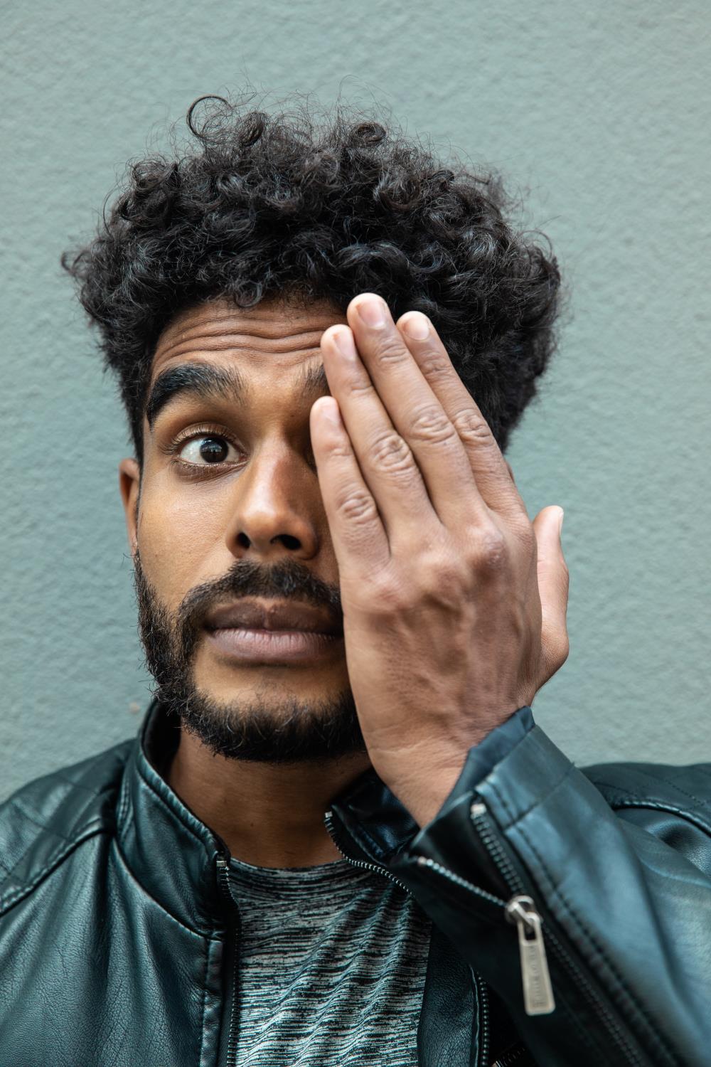 Mixed race man covering his left eye with his hand
